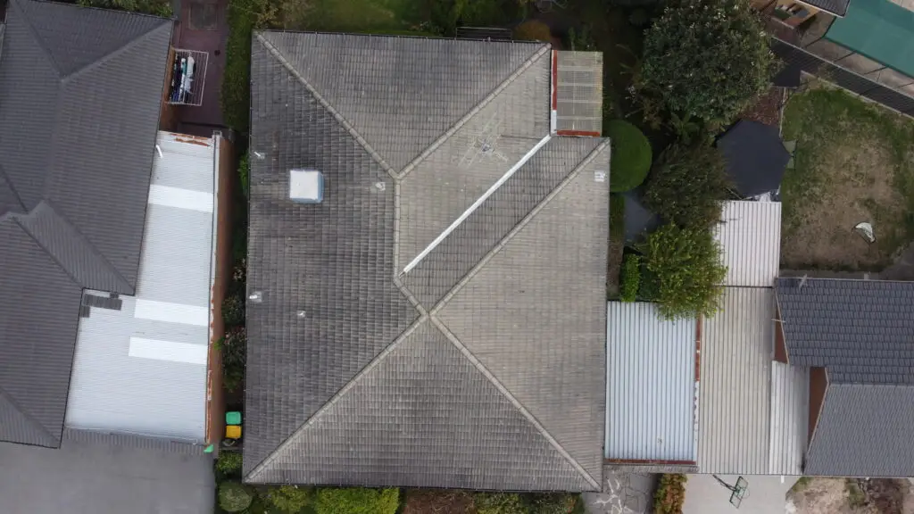 Aerial view of a large Melbourne home with a newly restored gray tile roof by Top Glaze Roofing Systems, surrounded by garden areas and a driveway, showcasing expert roof restoration services.