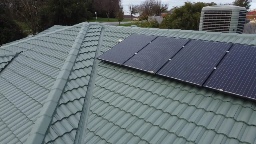 Four solar panels installed on a green tiled roof in Berwick by Top Glaze Roofing Systems, with trees and a roof vent visible—showcasing expert tile roof restoration and integration of solar solutions.