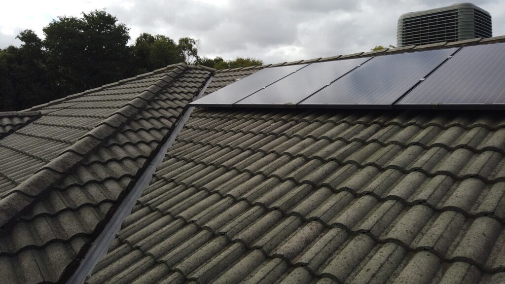 Restored gray tile roof in Berwick by Top Glaze Roofing Systems, displaying newly cleaned tiles, solar panels, and an air conditioning unit under a cloudy Melbourne sky.