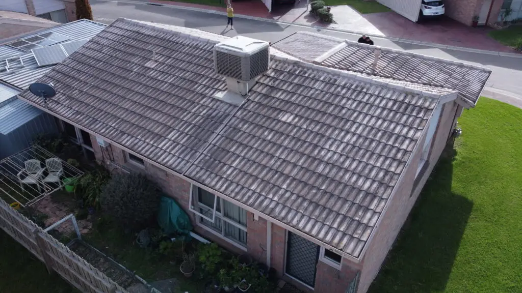 Aerial view of a Melbourne single-story brick home with a tiled roof in need of restoration, serviced by Top Glaze Roofing Systems. Surrounding features include green lawn, garden beds, patio area, and outdoor furniture.