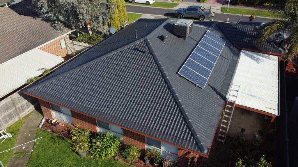 Aerial view of a single-story Melbourne home with a dark tiled roof featuring gutter guards and solar panels, showcasing Top Glaze Roofing Systems’ expert roof restoration services; garden surrounds the house, emphasizing a well-maintained property.
