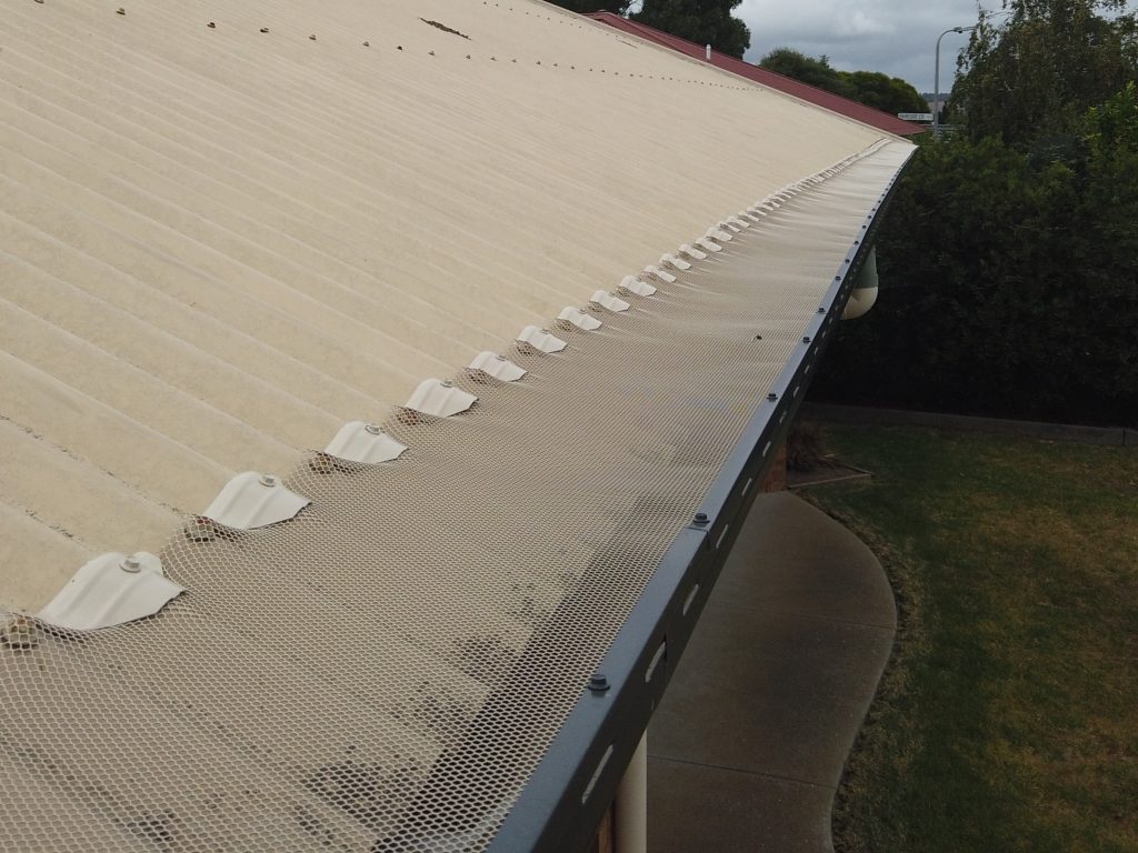 A beige metal roof with professionally installed Gutter Guards by Top Glaze Roofing Systems in Melbourne, protecting against debris buildup; surrounding trees and green lawn highlight the need for effective roof and gutter maintenance.