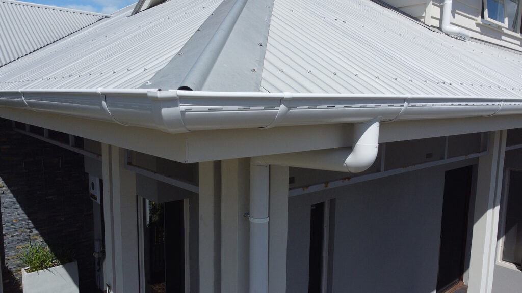 Close-up of a Melbourne home’s roof corner featuring newly installed white Colorbond metal roofing with matching gutters and downspouts by Top Glaze Roofing Systems, demonstrating expert roof replacement and gutter installation under a clear sky.