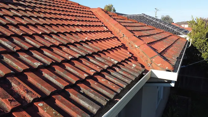 Close-up of a sloping Melbourne home’s roof with weathered, moss-covered red clay tiles needing roof repair or restoration by Top Glaze Roofing Systems, with white gutter visible.