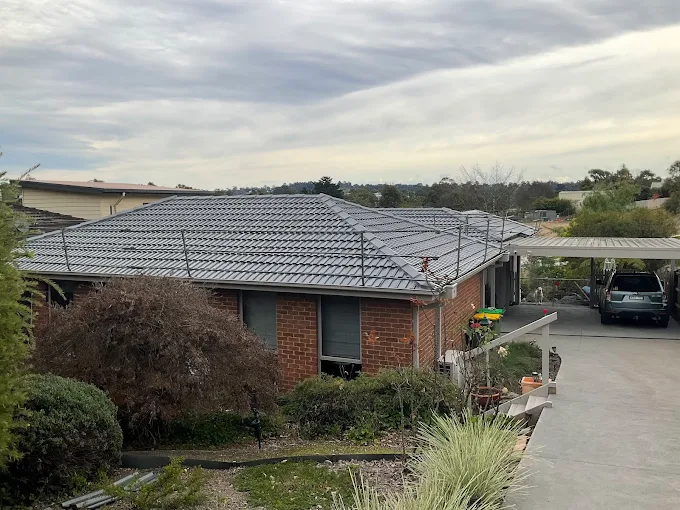 Single-story brick home in Melbourne featuring a gray tiled roof, perfect for showcasing Top Glaze Roofing Systems’ expert tile roof repair and restoration services, with lush green shrubs surrounding the property and an overcast sky indicating potential storm damage.