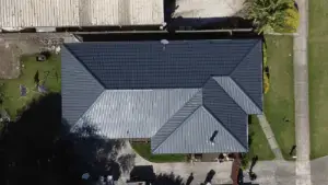 Aerial view of a house with a dark gray, gabled metal roof, surrounded by a driveway and lawn—ideal for a Services Single Post highlighting roofing or landscaping projects near similar buildings.