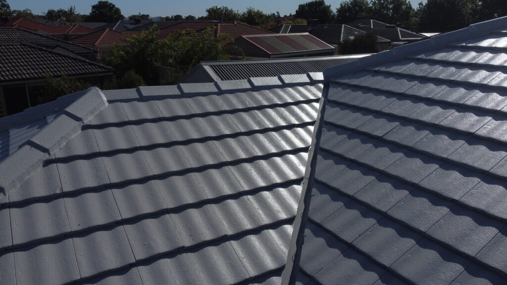 lose-up view of a freshly restored grey tile roof in Cranbourne with clean ridge capping, textured tile pattern, and neighbouring homes featuring red and charcoal roofs in the background.