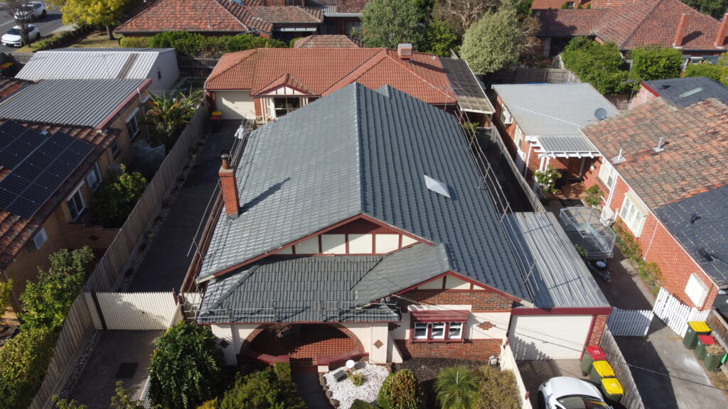 Angled aerial shot of a roof repair project in Bentleigh featuring a restored dark grey tiled roof with safety rails and skylight installation.