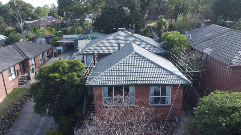 Aerial view of a tiled roof in Pakenham showing freshly repaired ridges and new tile alignment on a red brick home surrounded by greenery.