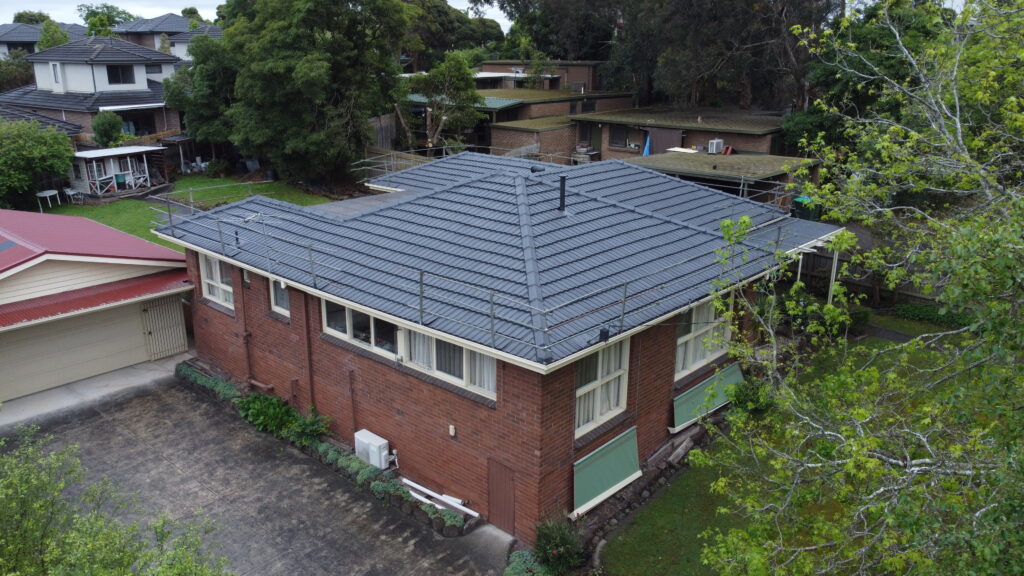 Corner view of a red brick home in Ringwood with newly repaired tile roof, scaffold safety rails, and a clean tile finish across all roof sections.