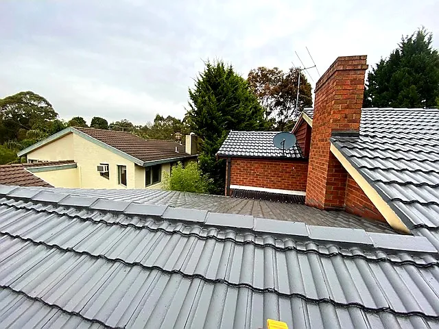 Tile roof repair on a Bayswater home, showing newly restored grey tiles and repointed ridge capping around chimney area.