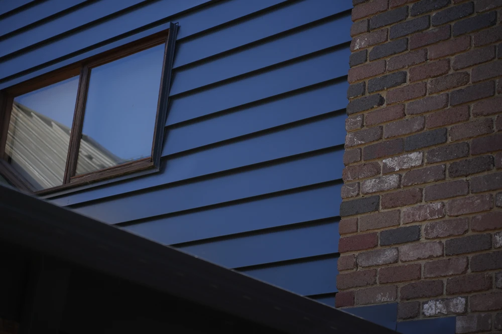Blue siding, open window, brickwork—Melbourne roofing repair and restoration.