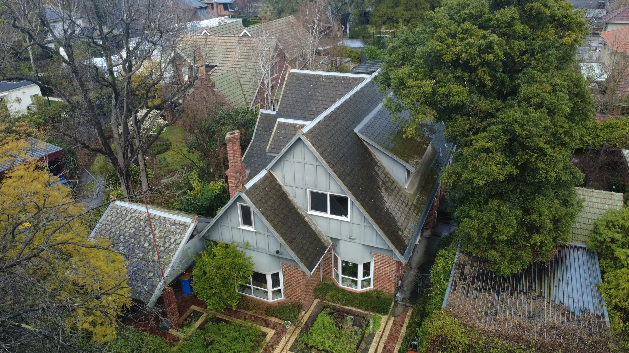 Melbourne house with steep, dark roof needing repair, aerial view.